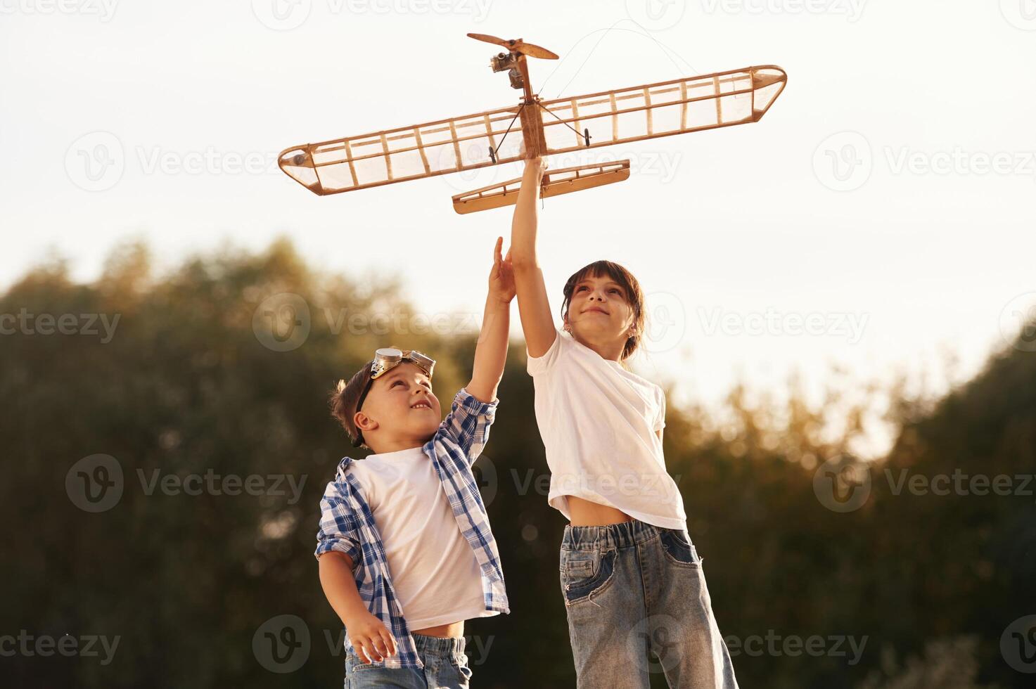 Boy and girl are playing with wooden toy plane on the field,, photo