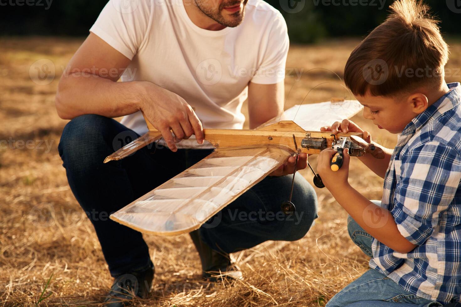 Messing ,around with,, broken toy. Father and son are with wooden plane on the field photo