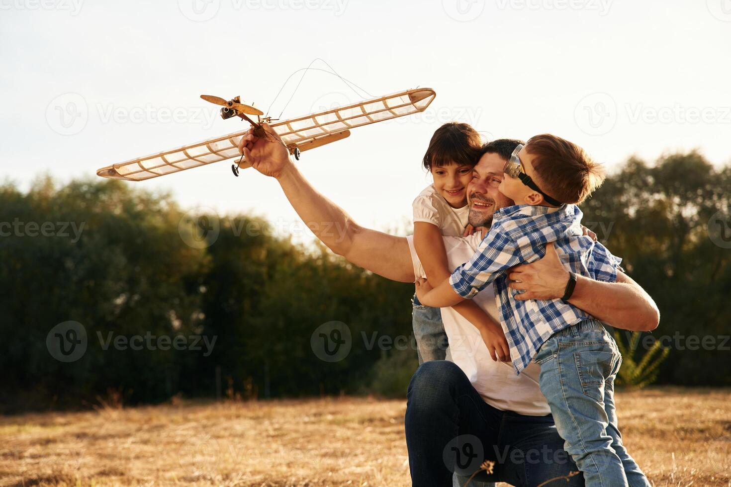 Sitting, side, view.... Family of father, son and daughter are playing with wooden toy plane on the field photo