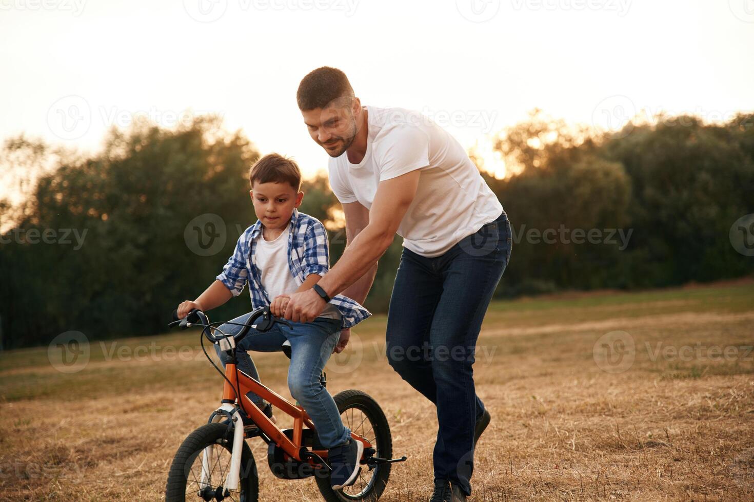 Teaching how to ride. Dad ,,with son are with bicycle on the field outdoors photo