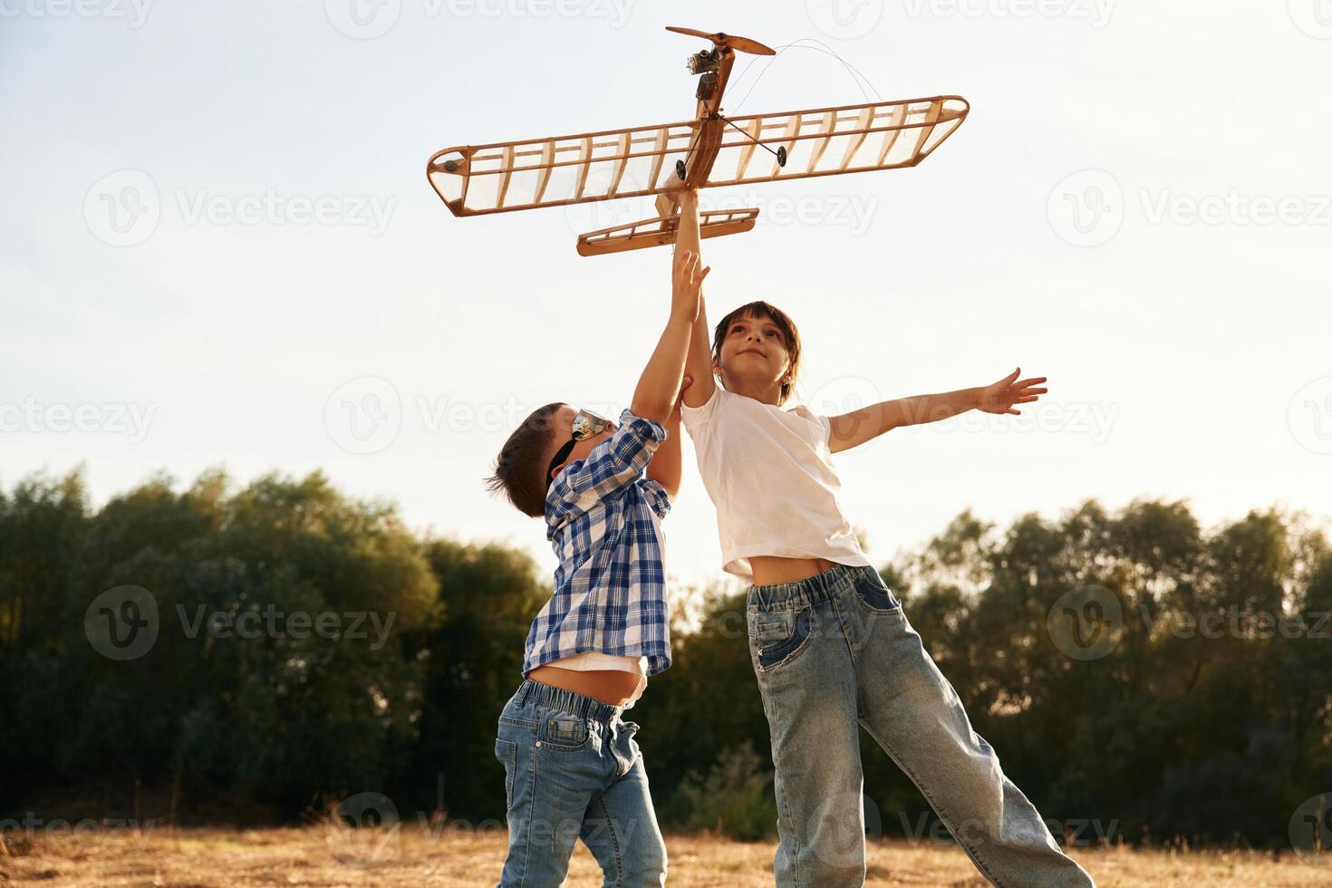 Flying high up. Boy and,, girl ,are playing with wooden toy plane on the field photo
