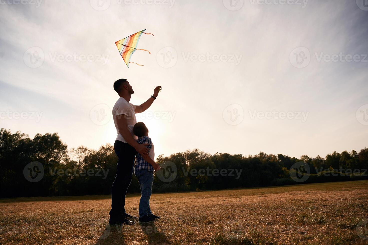 Father, and son are ,with kite on the field, illuminated by sunlight photo