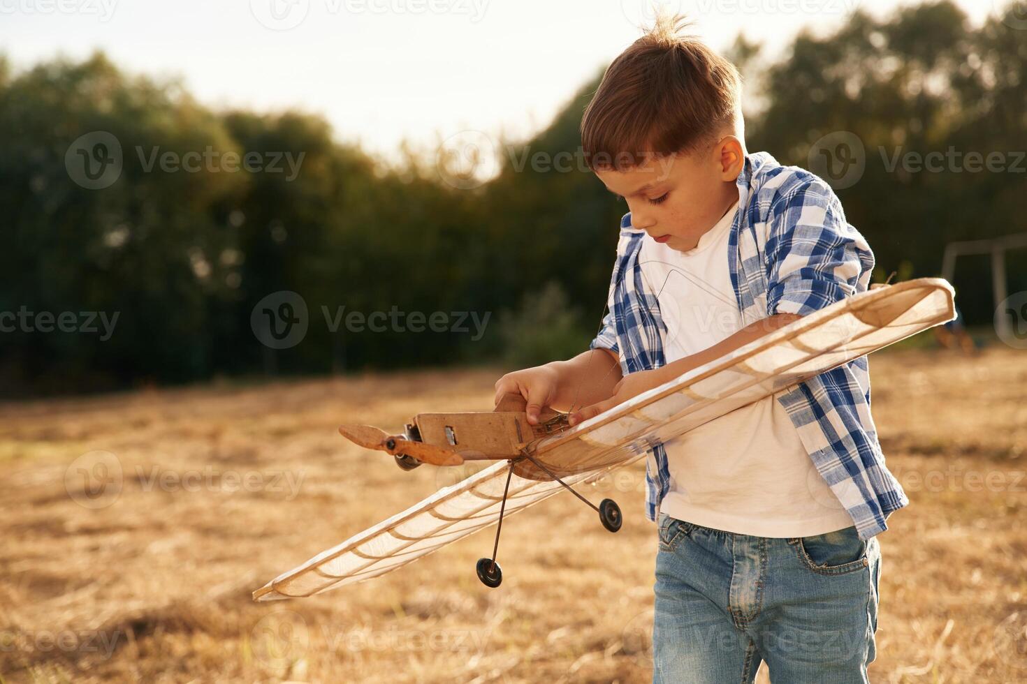 Fixing, the ,toy. Boy is playing with wooden plane outdoors on the field photo