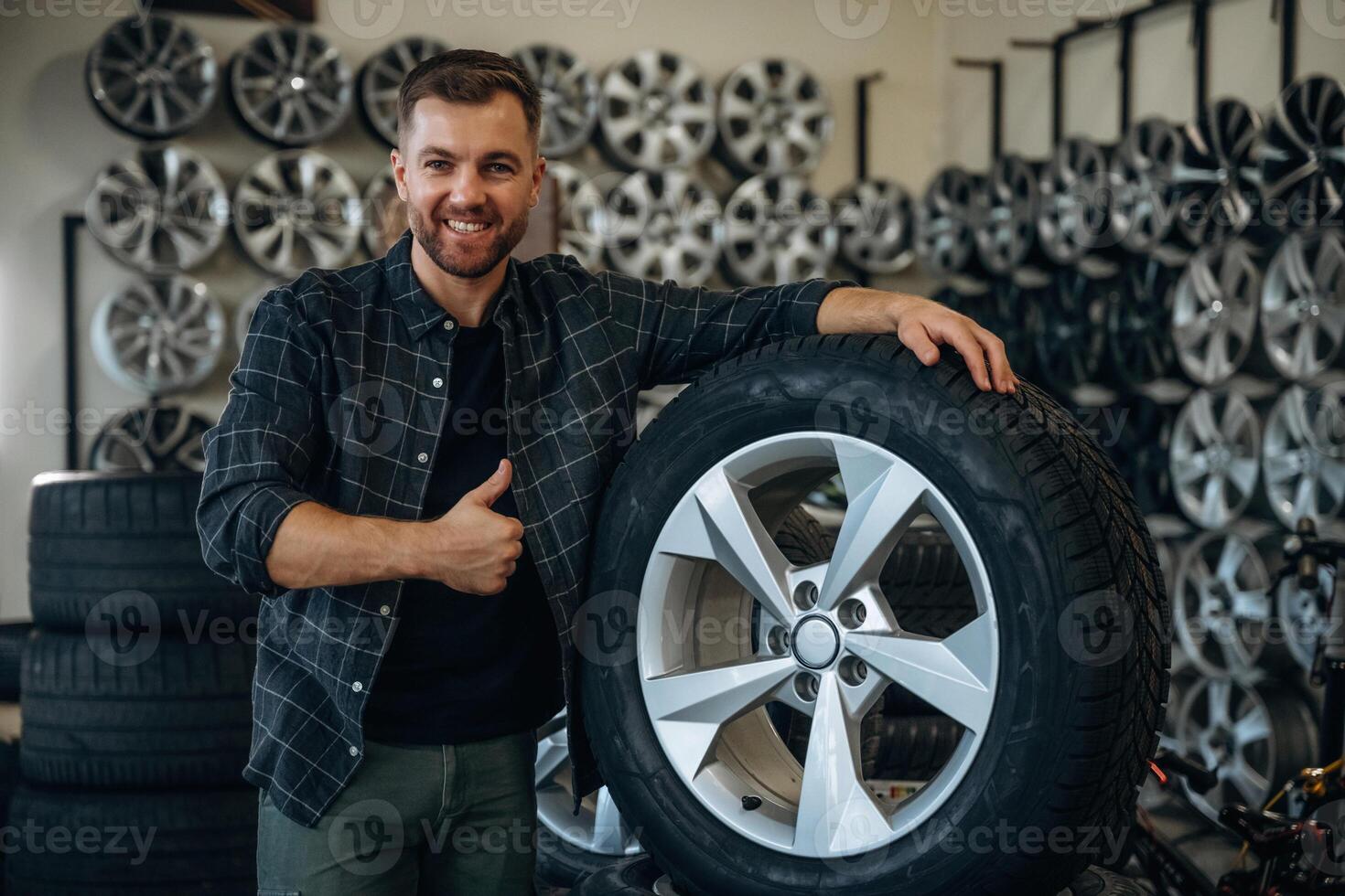 Smiling,, positive facial, expression,,, hand gesture. Man worker is maintenance station with tires, wheels photo