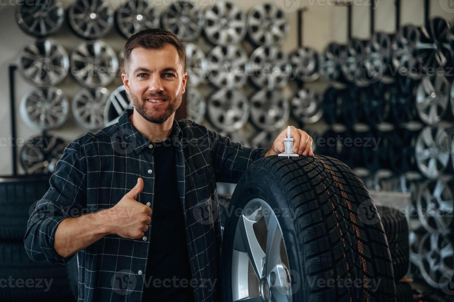 Smiling, positive facia,,,,l expression, hand gesture. Man worker is maintenance station with tires, wheels photo