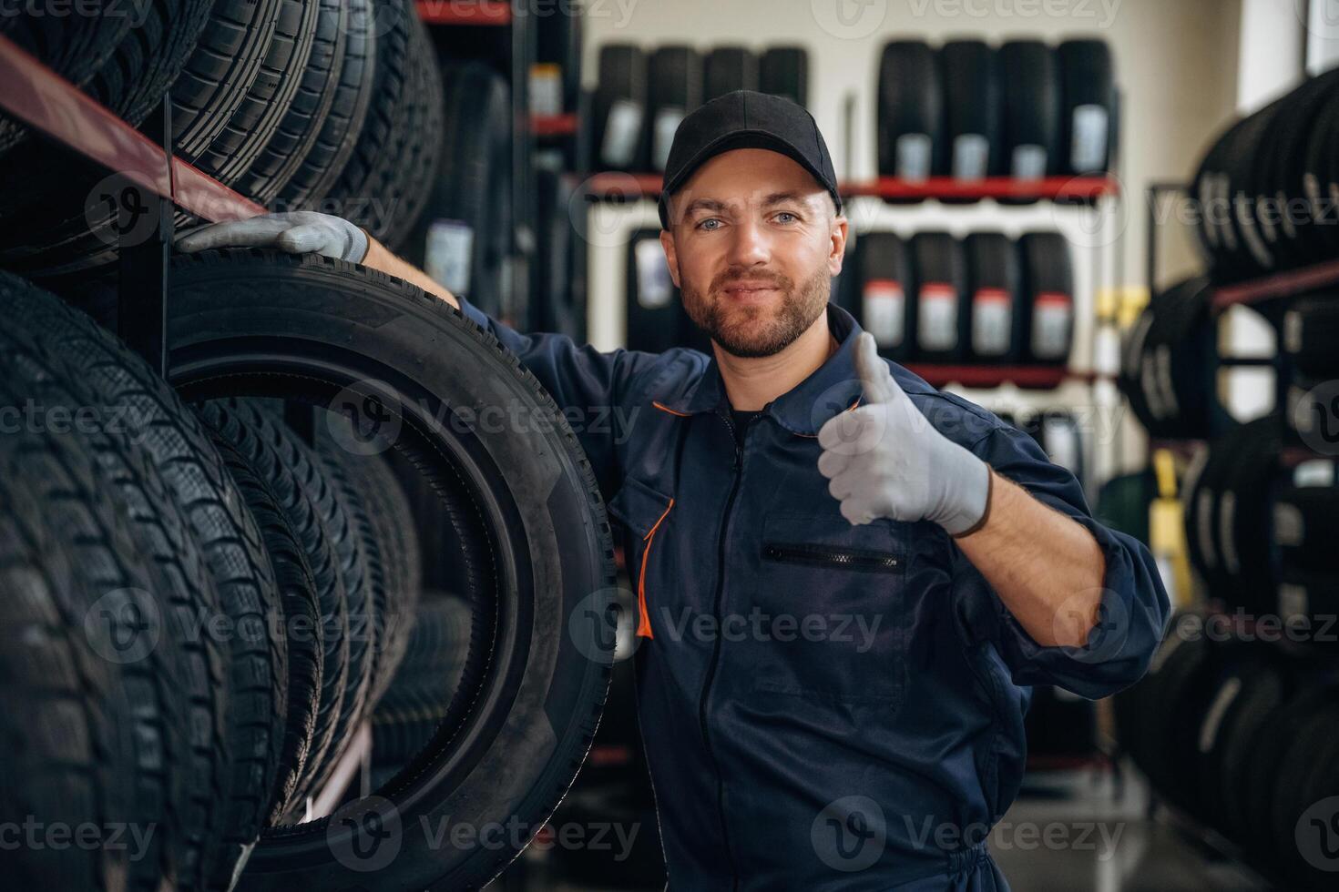 Friendly, facial ,,,,expression, in cap. Man worker is maintenance station with tires, wheels photo