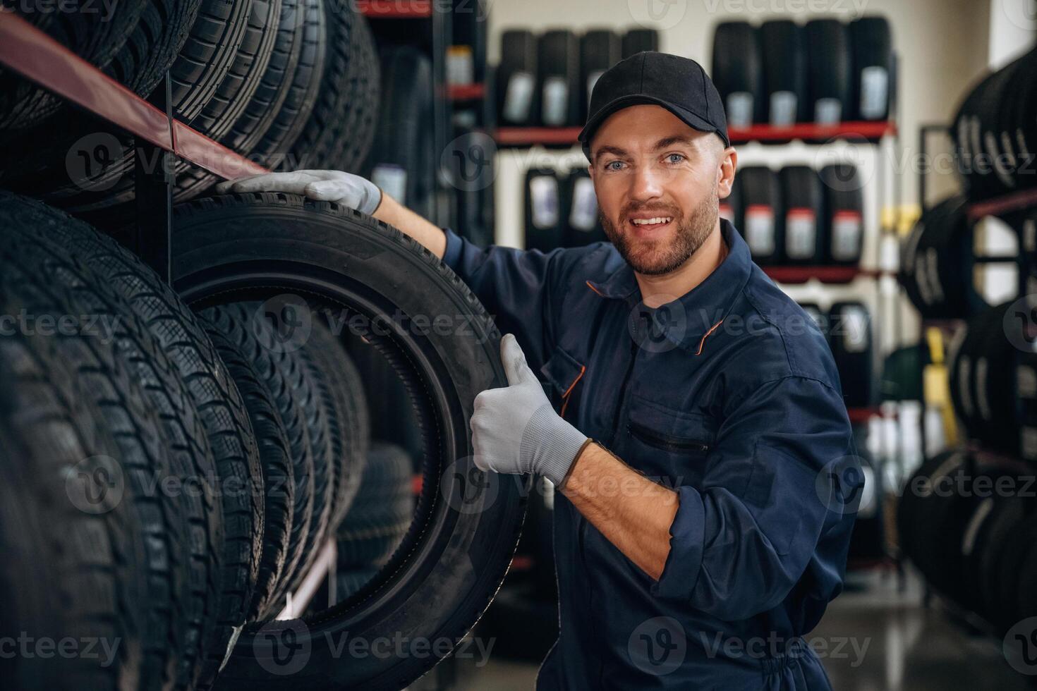 Friendly ,facial expression,,, in cap. Man worker is maintenance station with tires, wheels photo