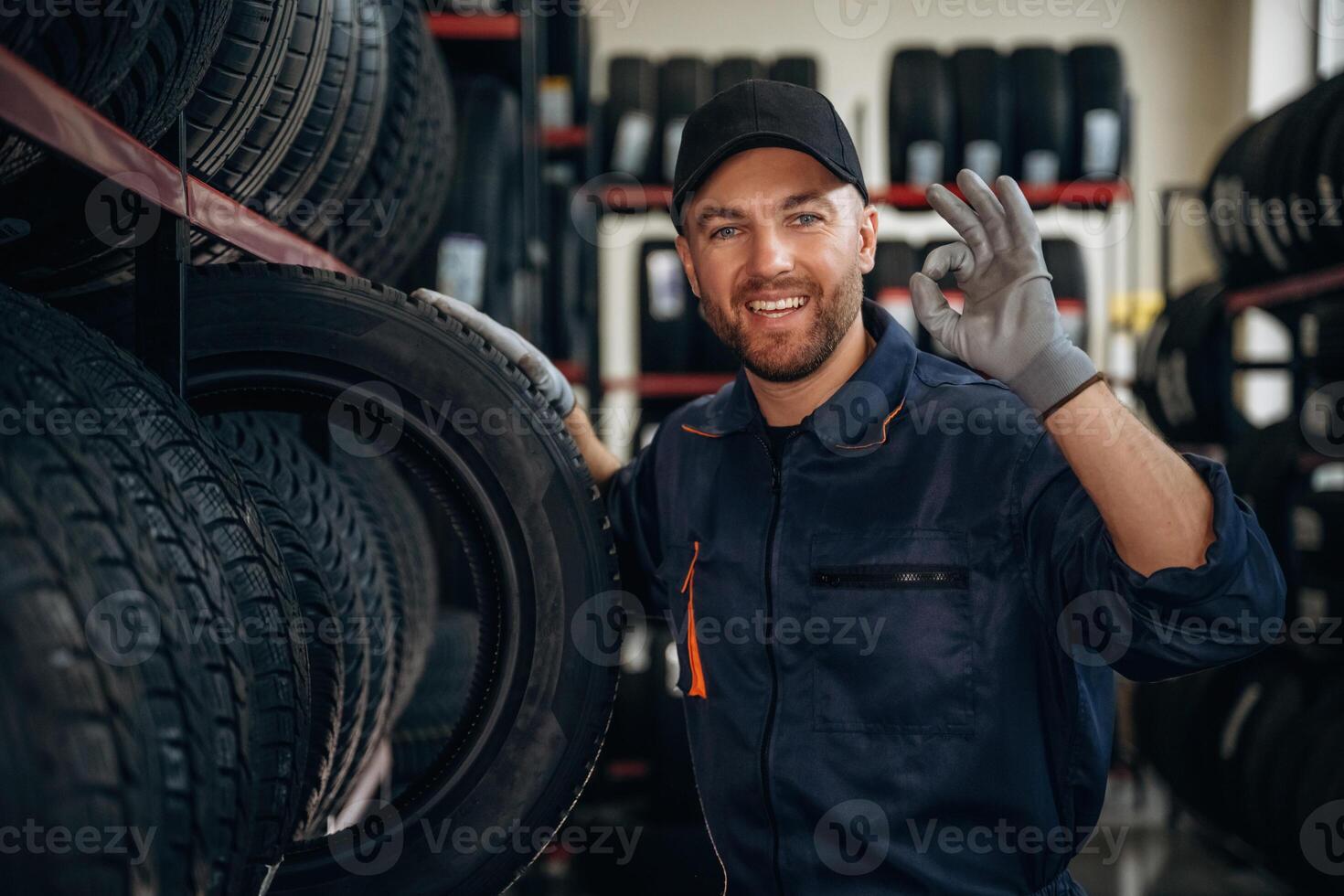 Friendly facial expression,, in, cap.. Man worker is maintenance station with tires, wheels photo