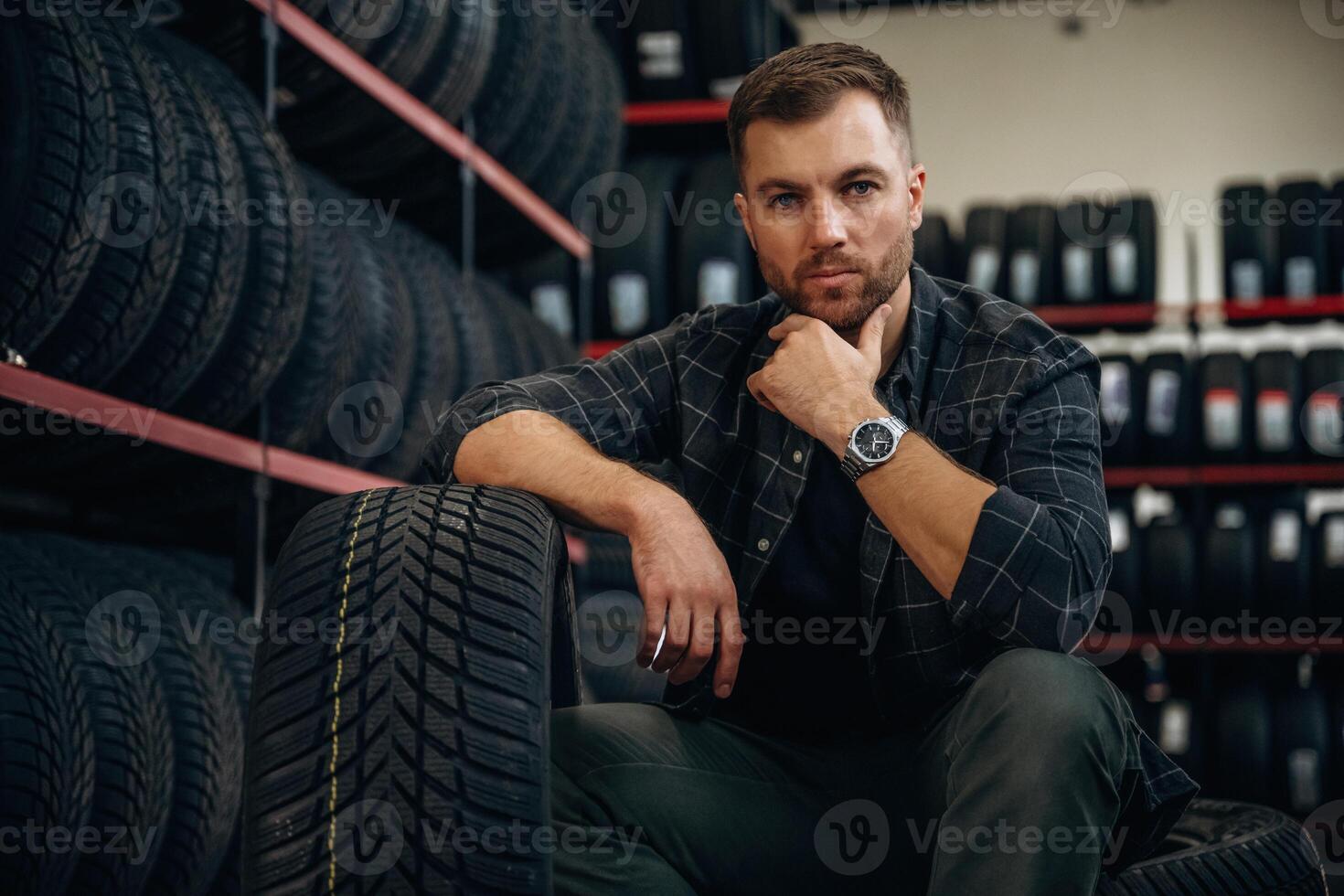 Thinking,, sitting. Man worker is maintenance station with tires, wheels photo