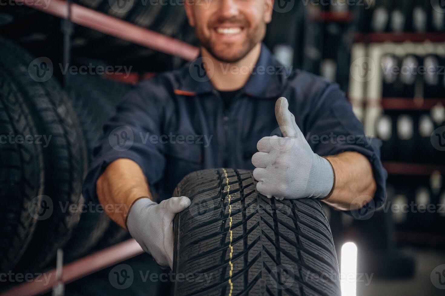 Focused close up view,,,, thumb up, holding a tire. Man worker is maintenance station with wheels photo