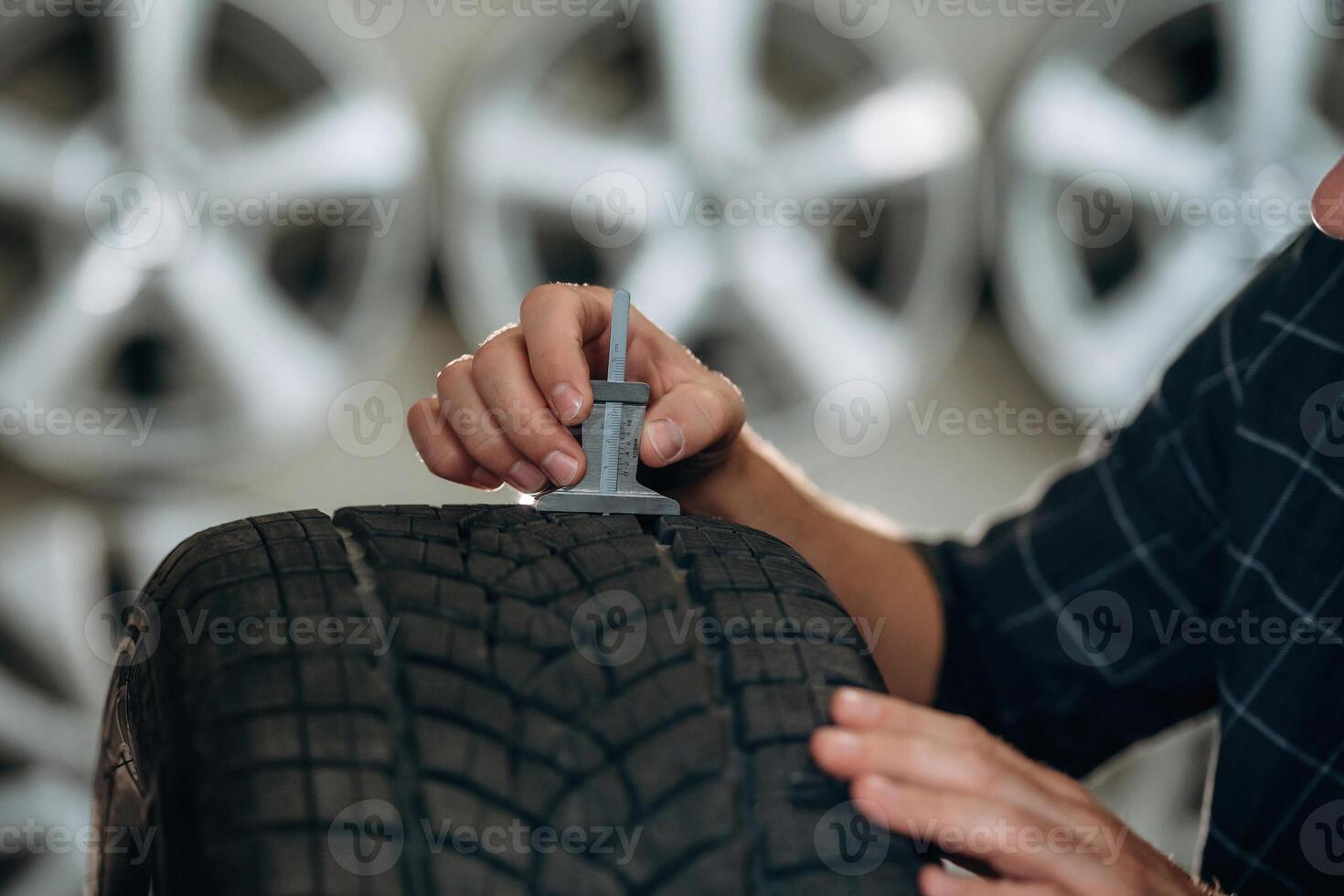 With measuring tool. .Man worker is maintenance station with tires, wheels photo
