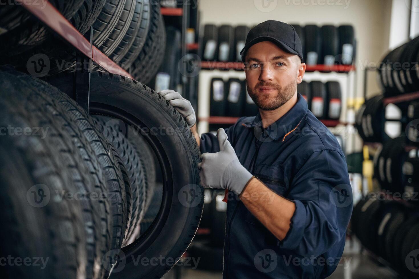 Friendly,, facial, expression, in cap. Man worker is maintenance station with tires, wheels photo