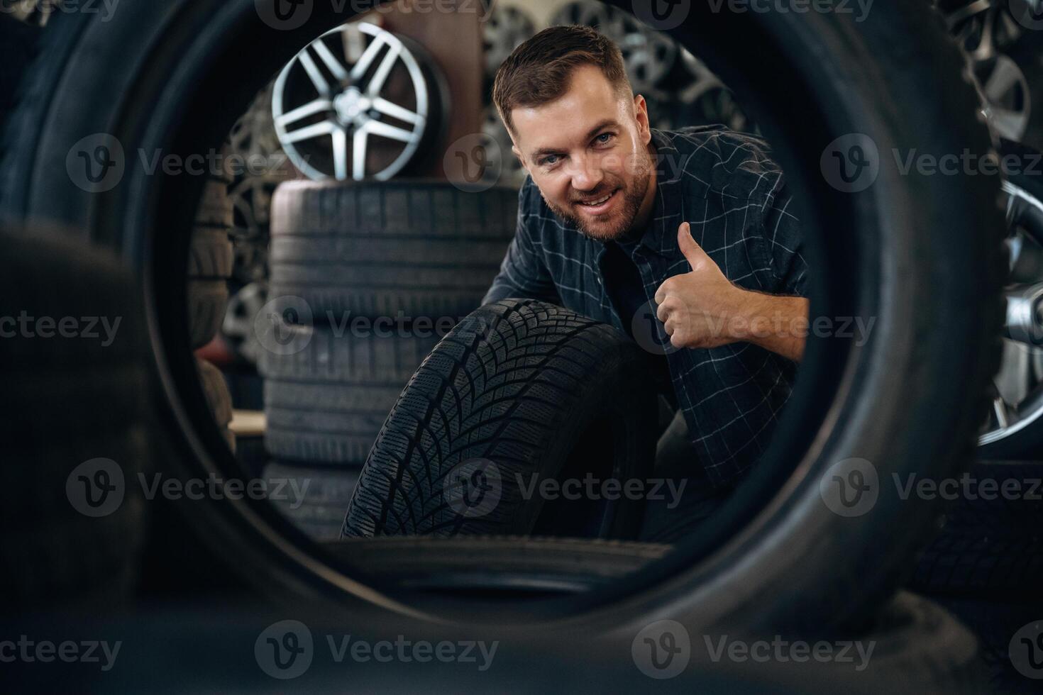 Smiling,,, positive facial expression, hand gesture. Man worker is maintenance station with tires, wheels photo