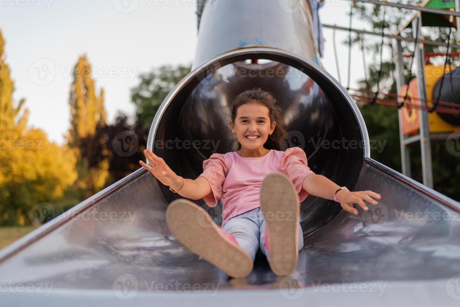 A happy child girl playing on a slide on the park playground. photo