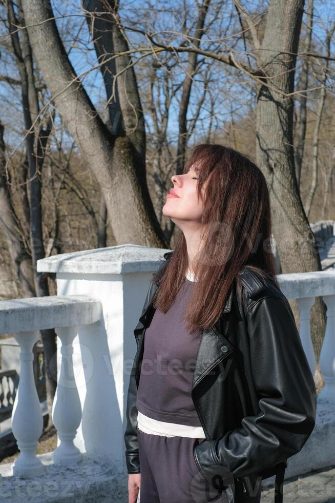 Woman enjoying the sunny day while gazing towards the sky among bare trees in a serene outdoor setting photo
