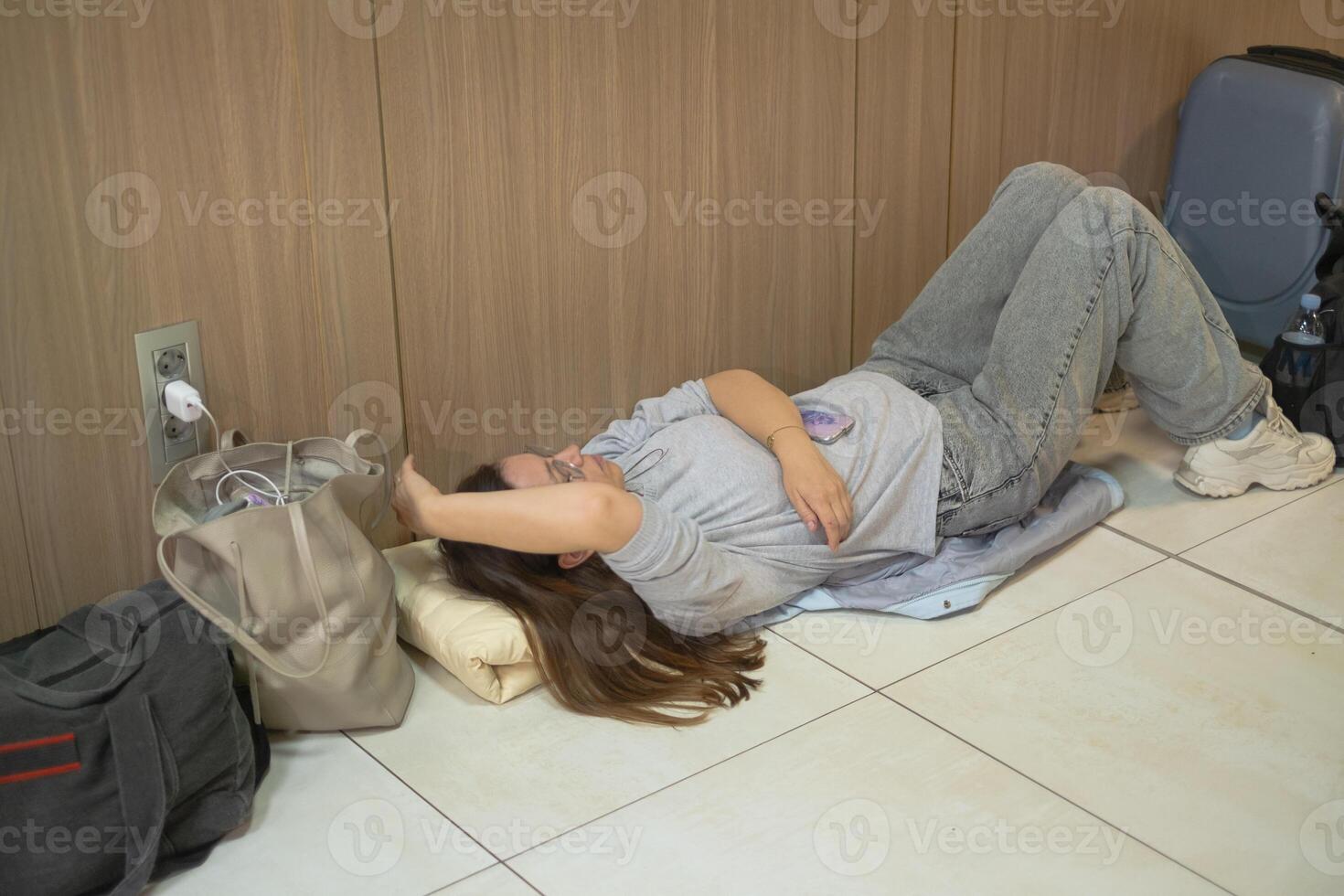 Travelers resting on the floor of an airport terminal as their journey awaits in a crowded travel hub at late night photo