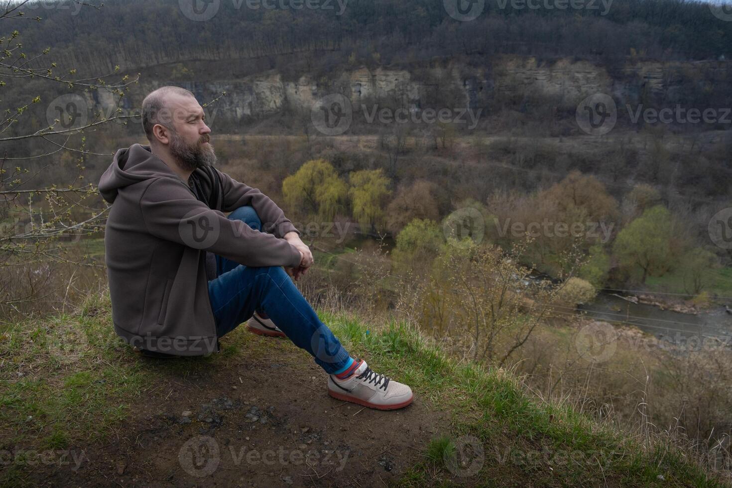 Man sits quietly by a riverbank overlooking a serene landscape in early spring photo