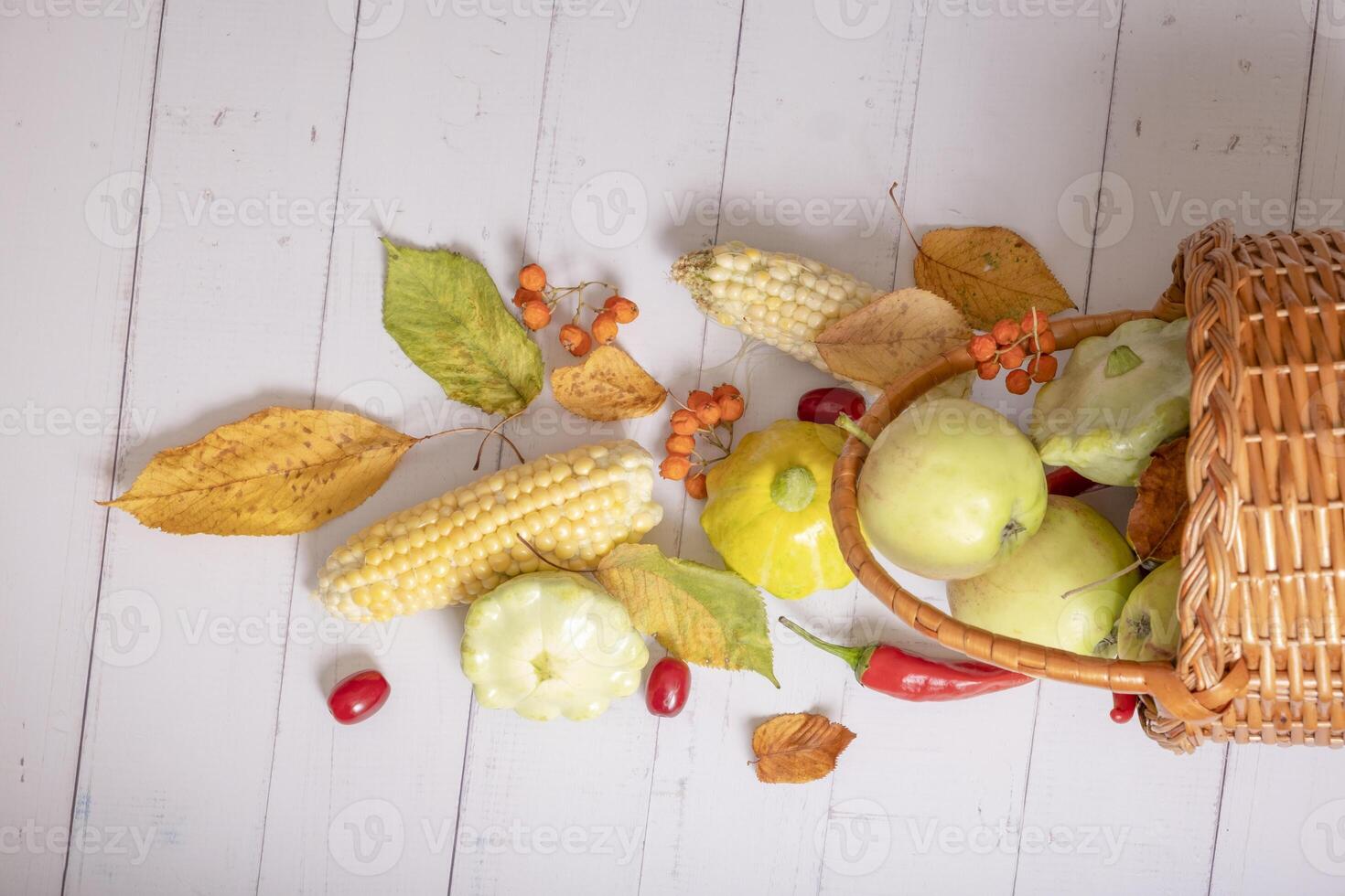 Top view autumn harvest basket with corn, apples, zucchini and peppers on a wooden background decorated autumn leaves photo