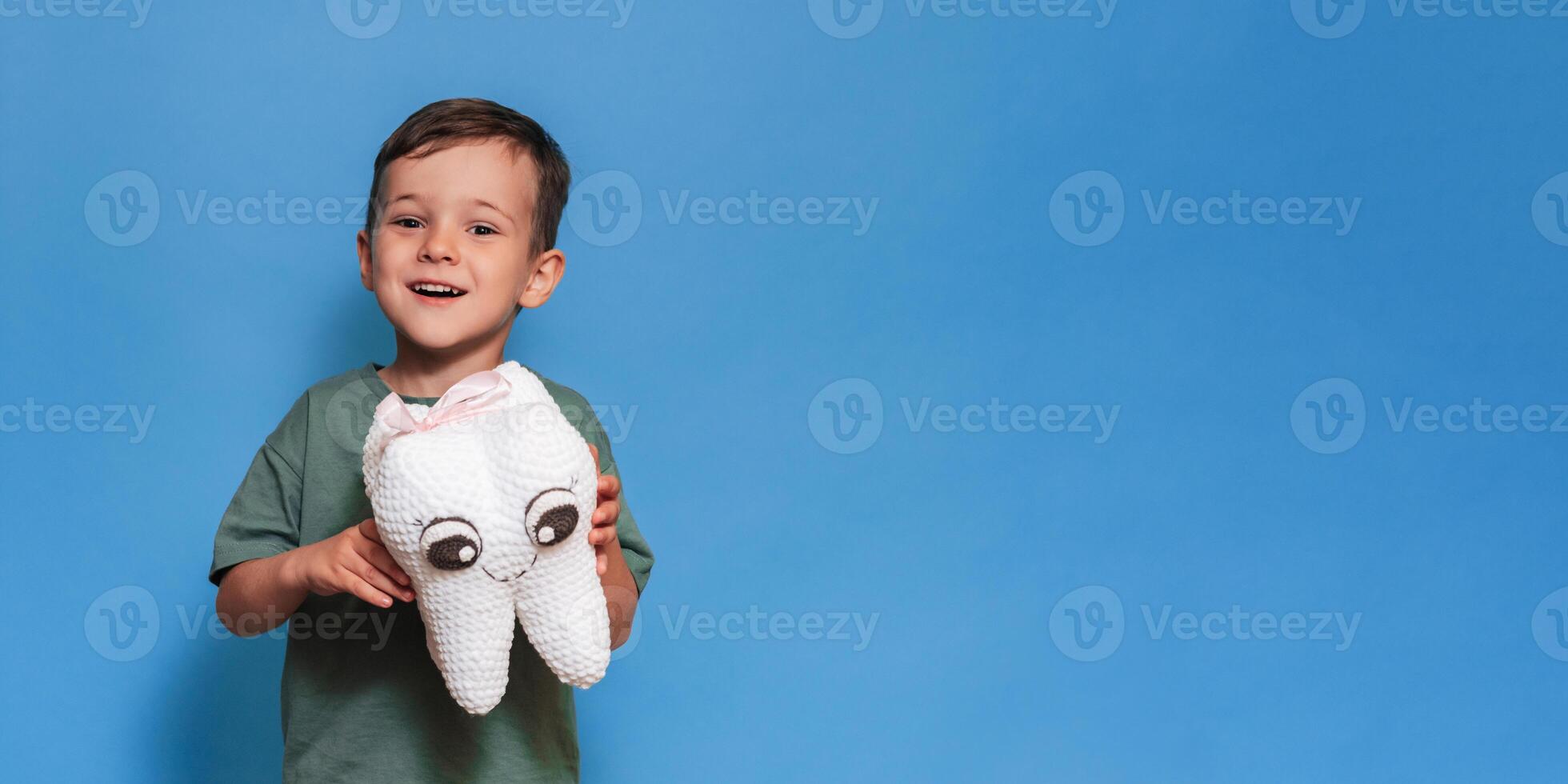 A smiling boy with a plush tooth on a blue background. Pediatric dentistry. A place for your text. Panoramic photo. photo
