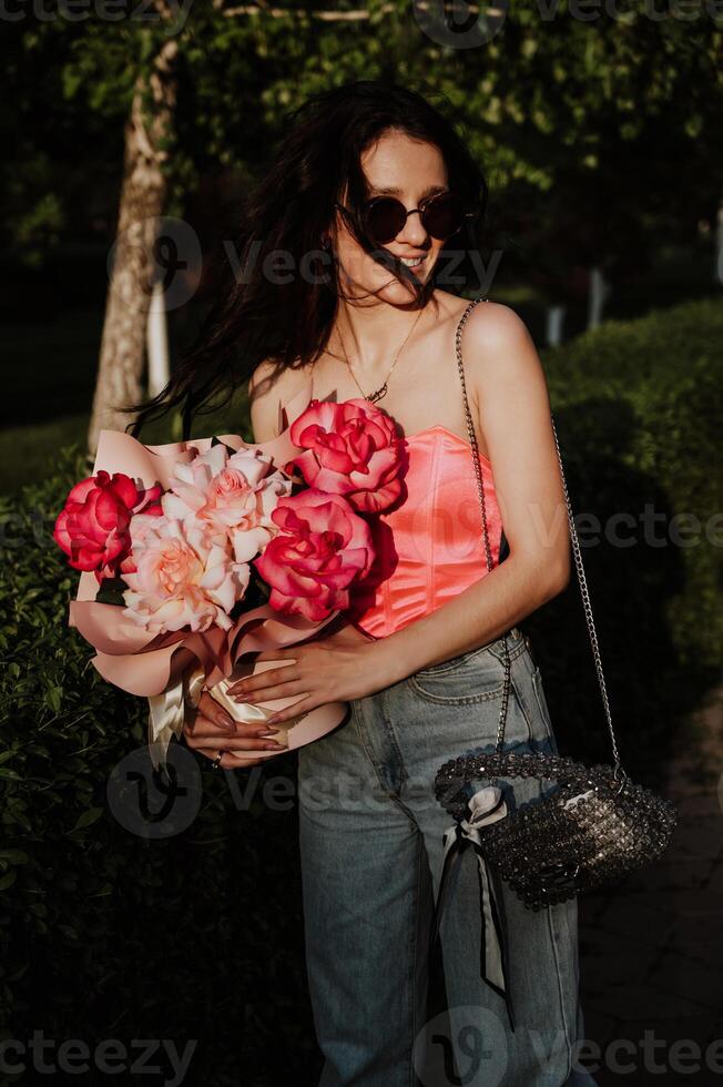 Portrait of a beautiful young woman in close-up holding a bouquet of roses in a park in summer photo