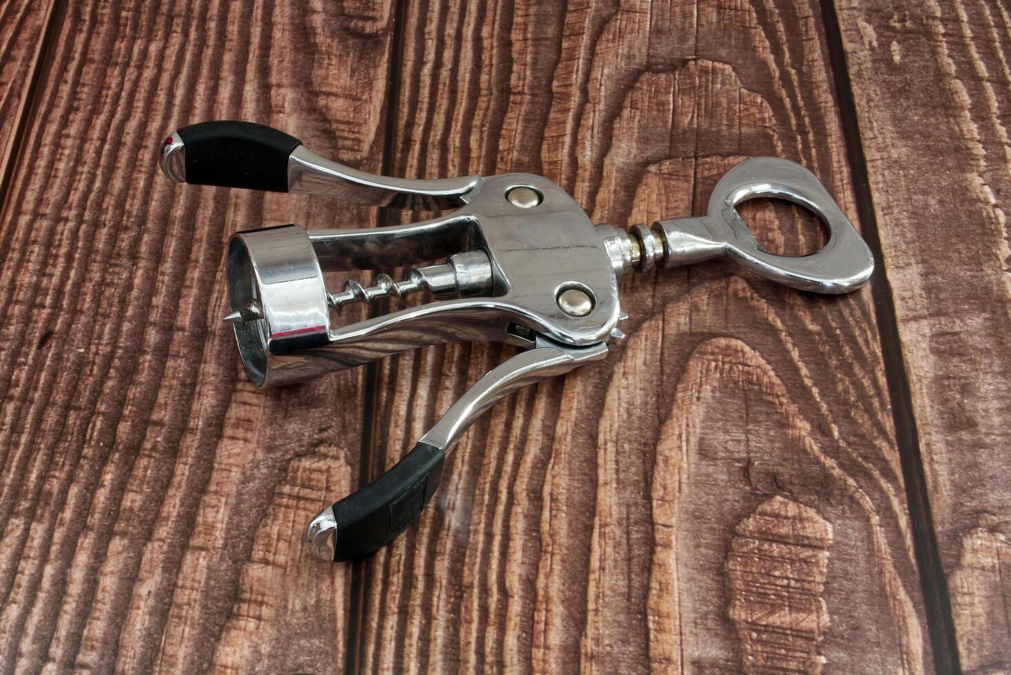 Shiny metal corkscrew wine opener tool with black handles sitting on rustic wooden table surface photo