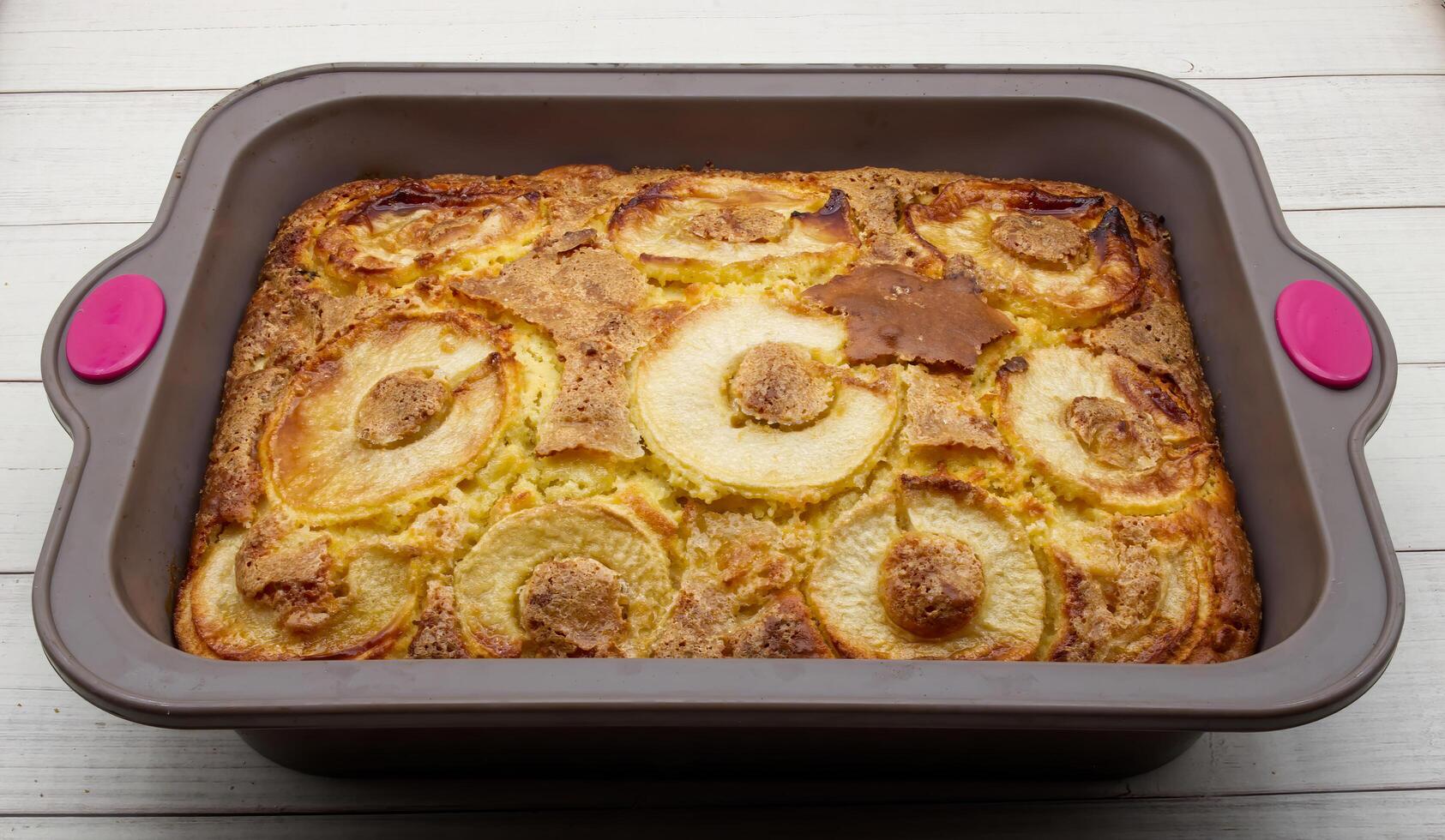 Delicious homemade baked apple cake in a rectangular baking pan resting on a rustic white wooden surface photo