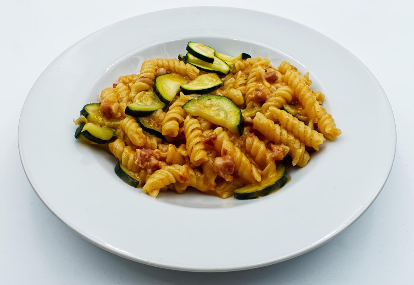 Delicious fusilli pasta dish served with fresh zucchini slices on a white plate background photo