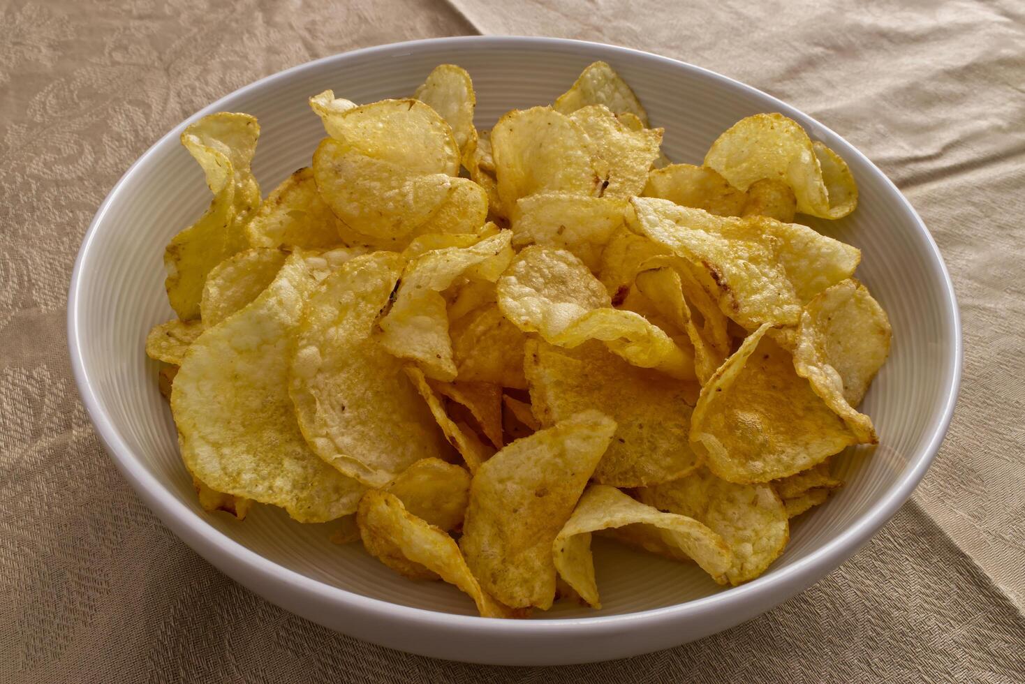 Crispy potato chips piled high in a white bowl. photo