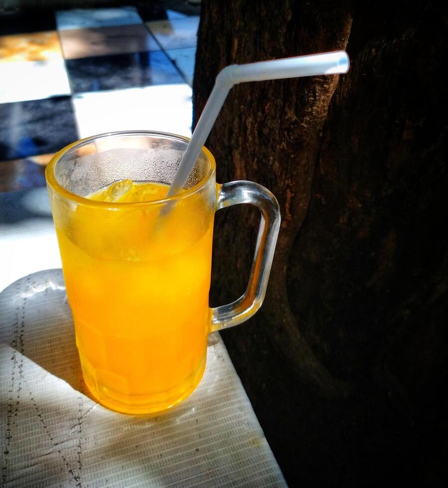 A glass of orange juice with a straw in it. The glass is half full and the straw is in the middle of the glass photo