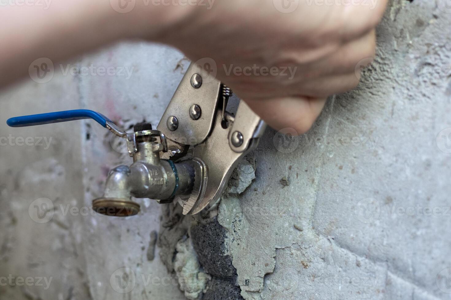 A man uses an adjustable wrench to tighten a metal faucet on a concrete wall photo