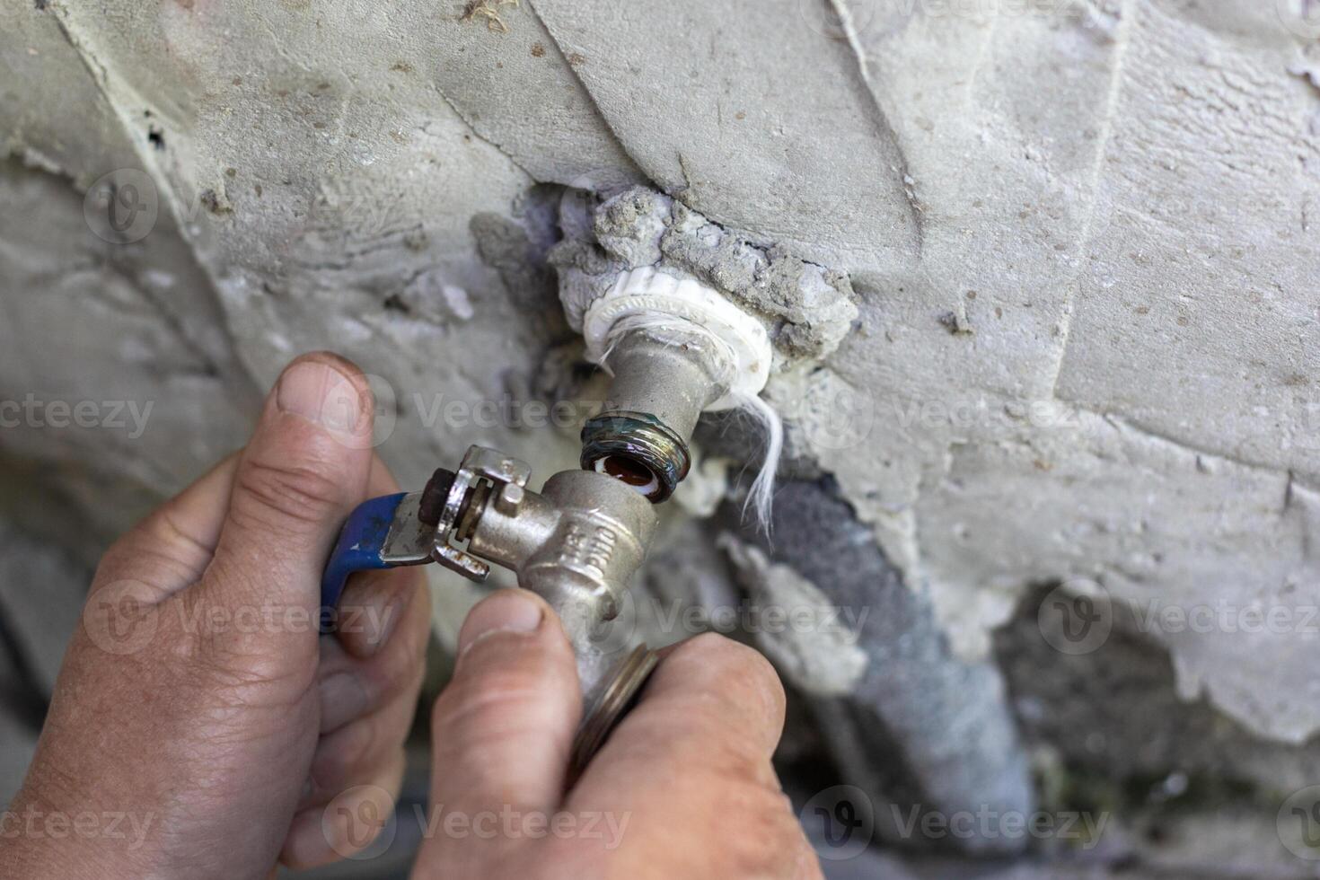 male hands installing a metal faucet on a cracked concrete wall photo