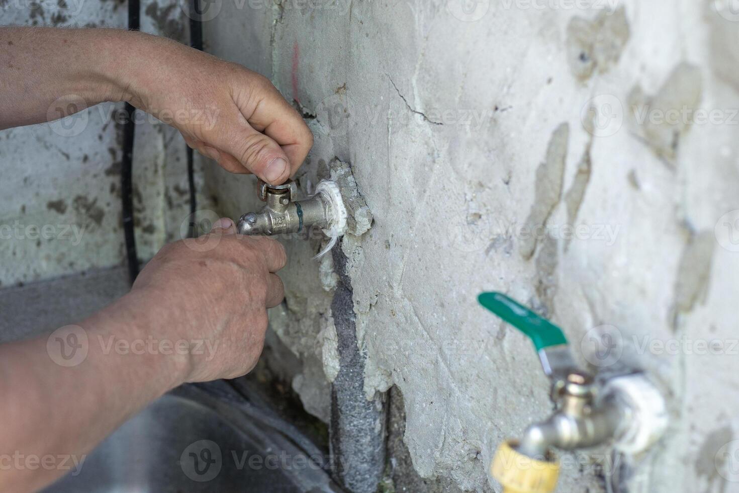 man repairs a faucet by tightening it on an old wall with a wrench photo