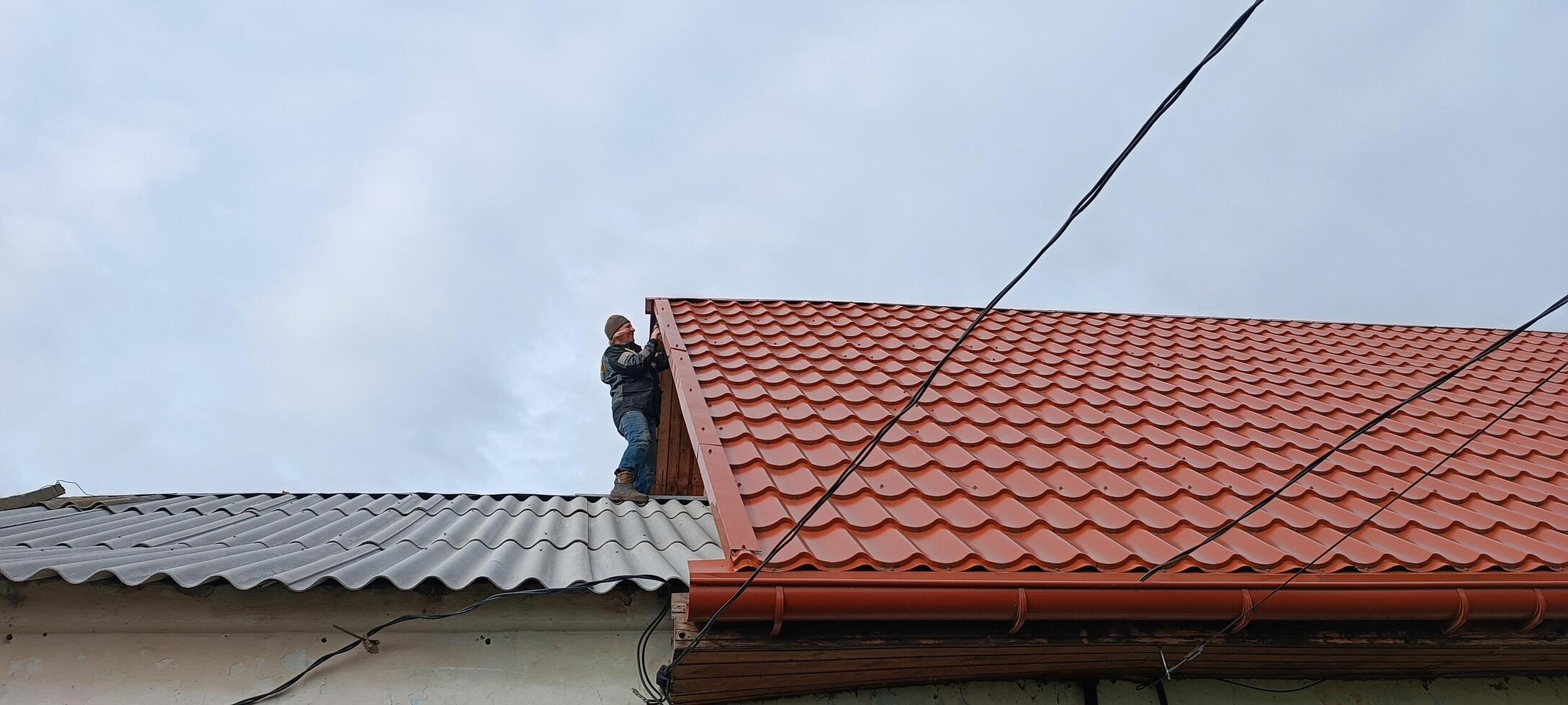 A man climbed onto the roof examining the gable at the junction of the multi-level roofs of a village house. Mobile photo