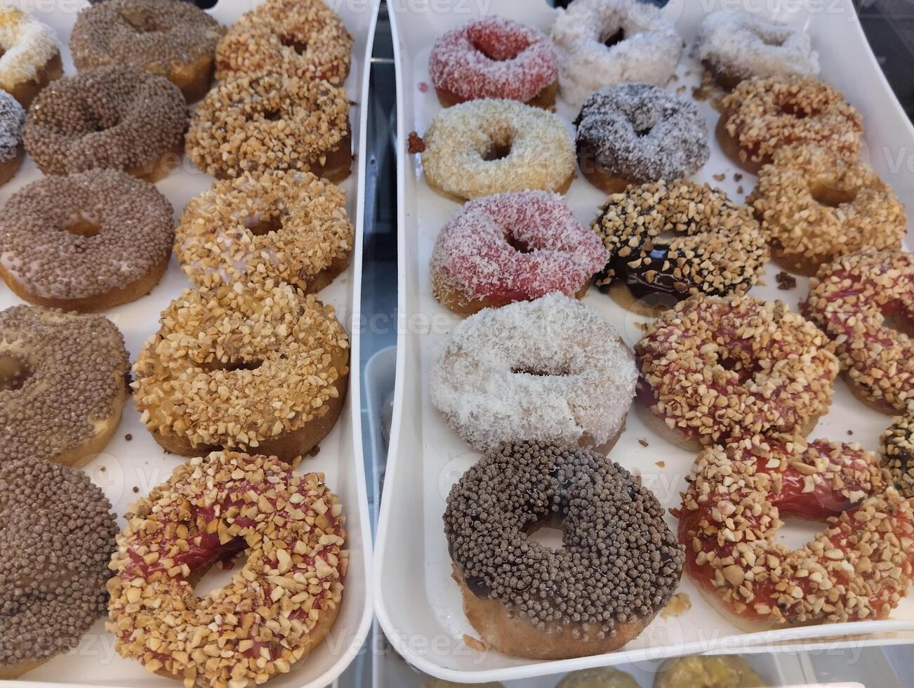 Donuts in colored glaze in chocolate with sprinkles of nuts puffed rice are on a tray. Virina Ponchikova. Takeaway photo