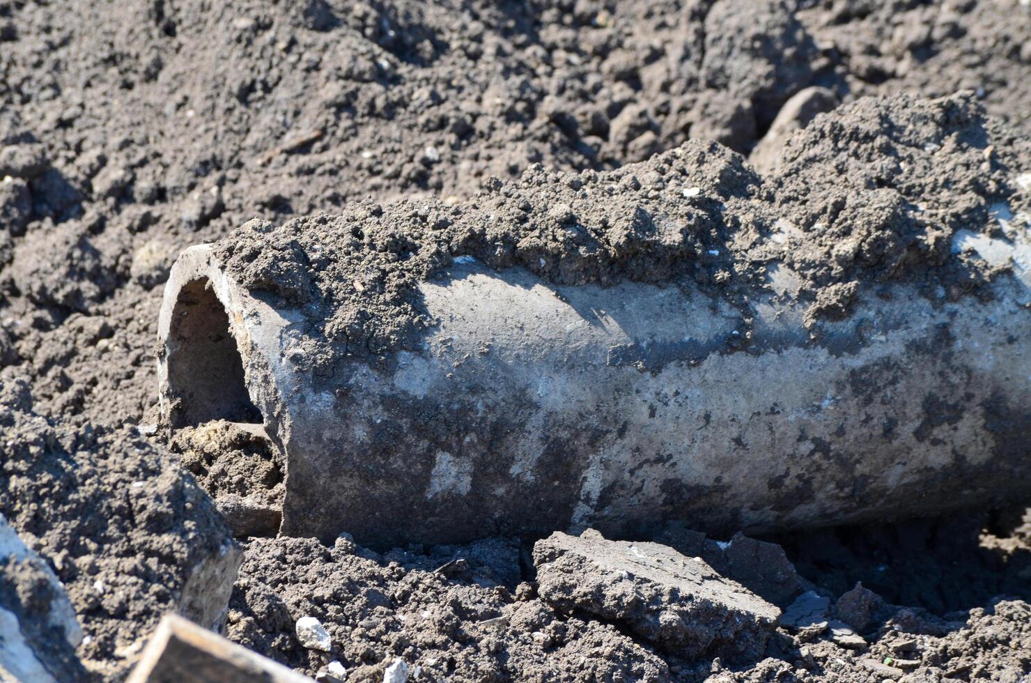 A pipe is laying on the ground in a pile of dirt. The dirt is brown and the pipe is gray. The image has a somewhat somber mood, as the pipe is broken and abandoned photo
