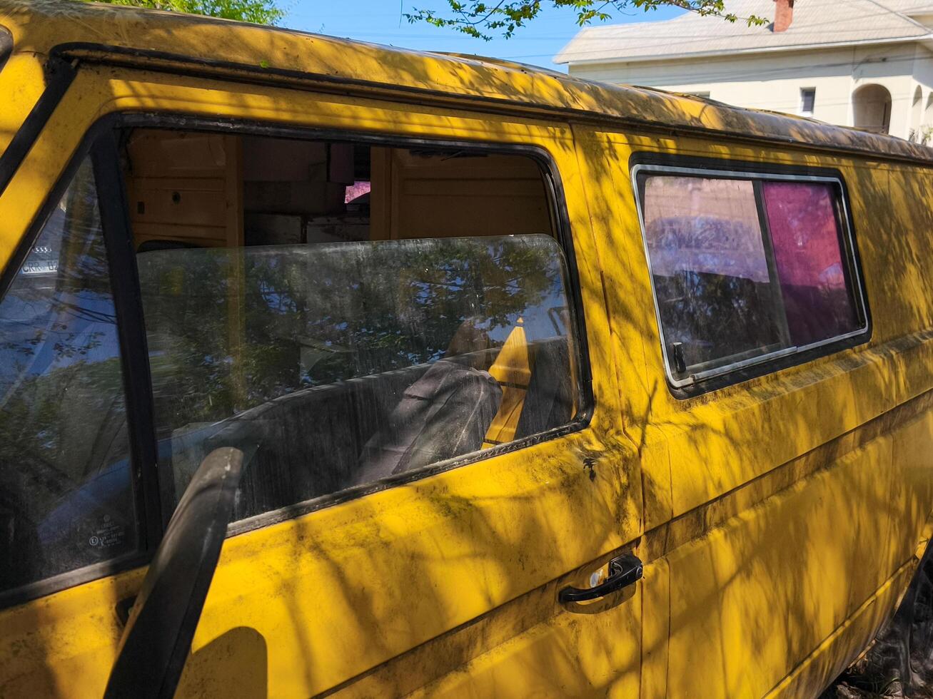 A yellow van with a red window. The van is parked in front of a house. The van is dirty and has a worn-out appearance photo