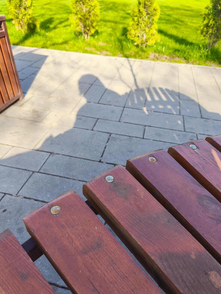 A wooden bench with a woman's shadow on it. The bench is on a patio with a brick floor photo