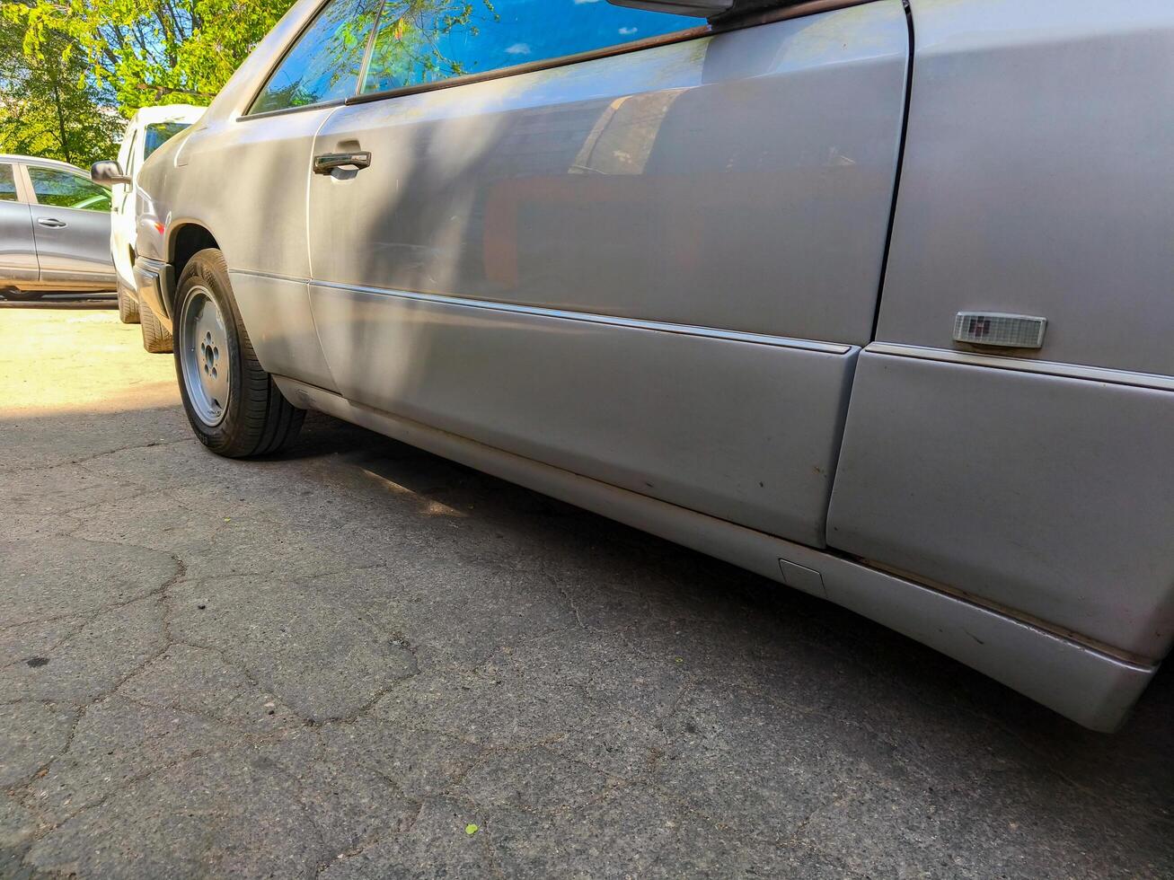 A silver car with a white stripe on the side. The car is parked in front of a white car photo