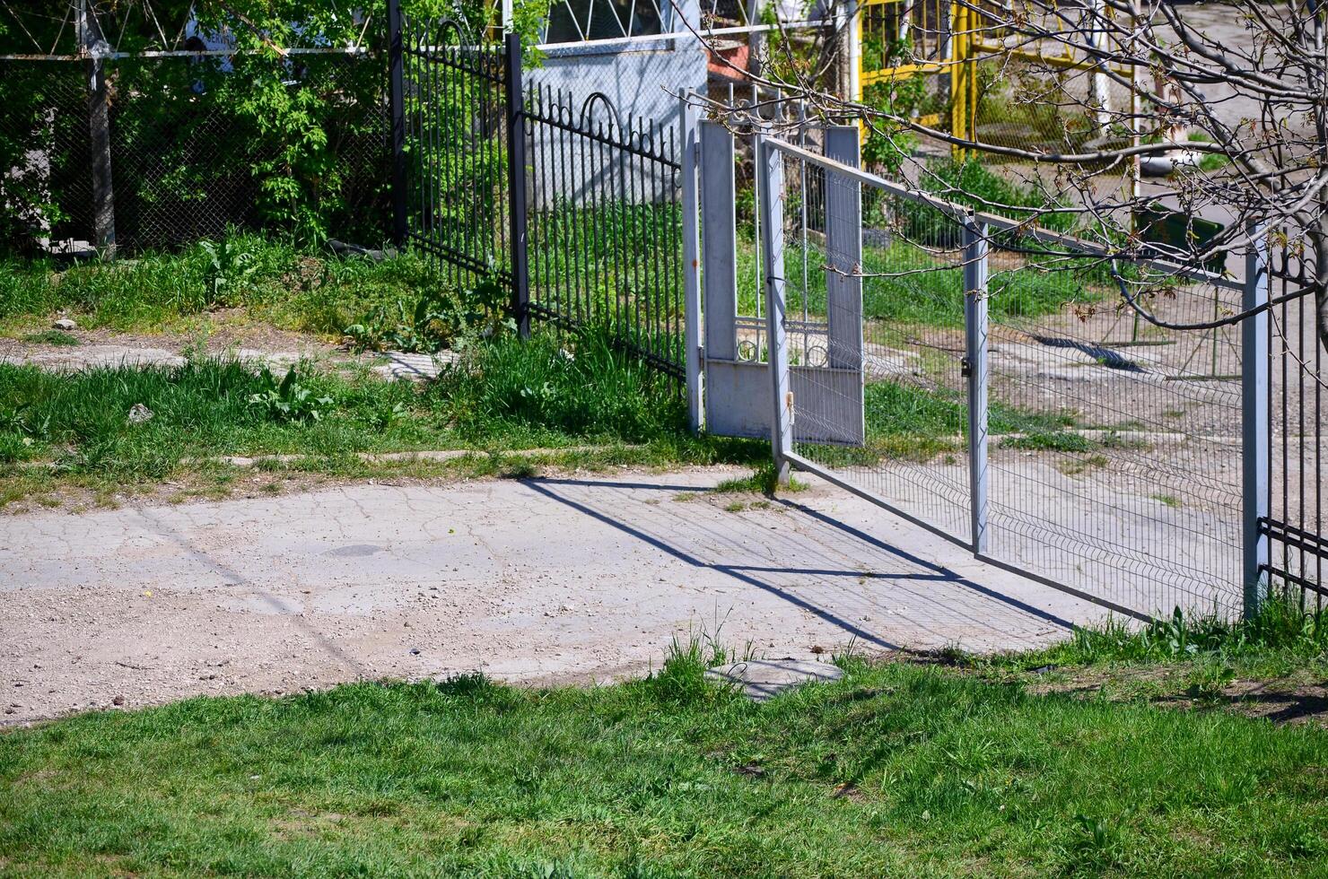 A gate is open in a yard with a fence behind it. The gate is made of metal and is open to the right. The yard is surrounded by a fence and has a lot of grass photo