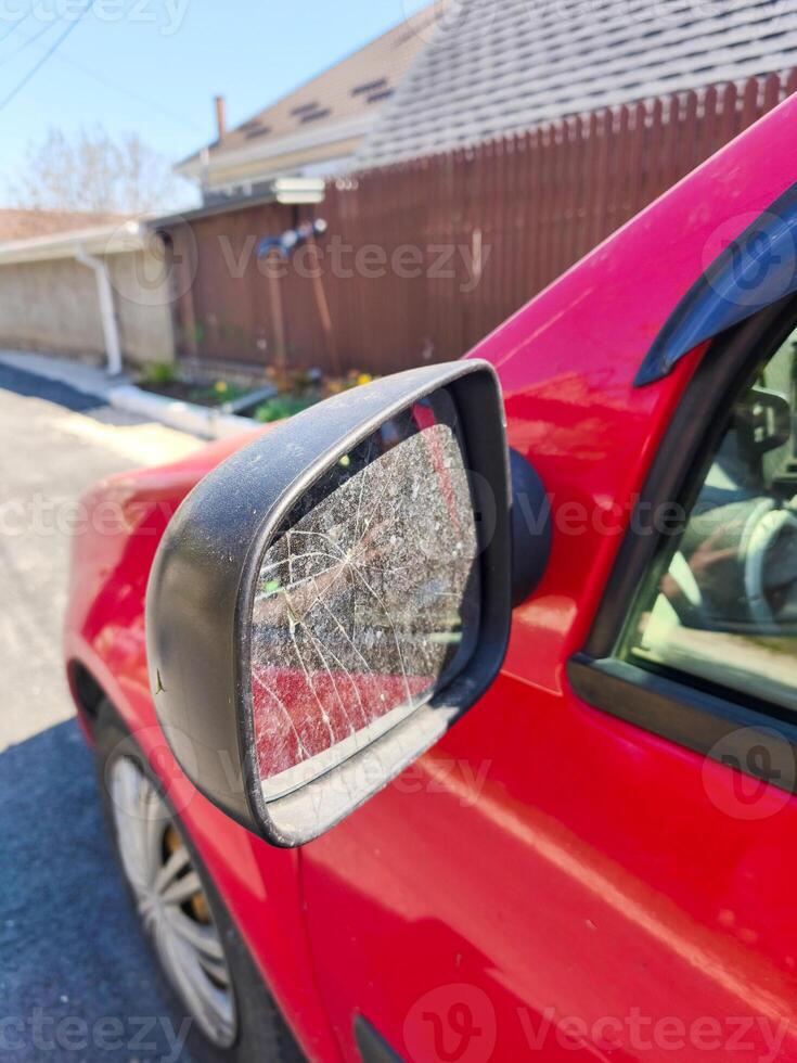 A red car with a dirty mirror. The mirror is cracked and has a lot of dirt on it photo