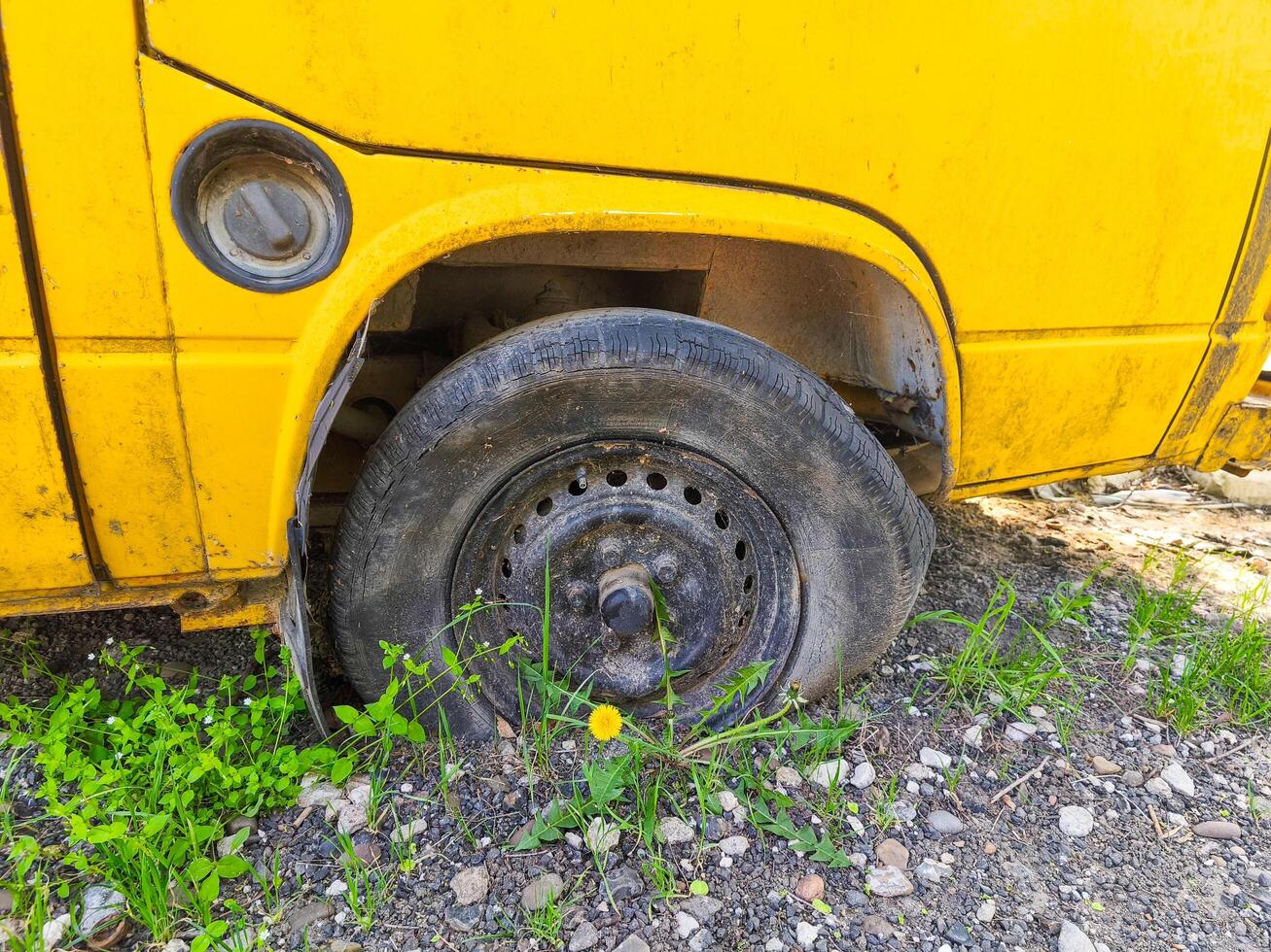 A yellow school bus with a flat tire. The tire is missing and the bus is parked on a dirt road photo