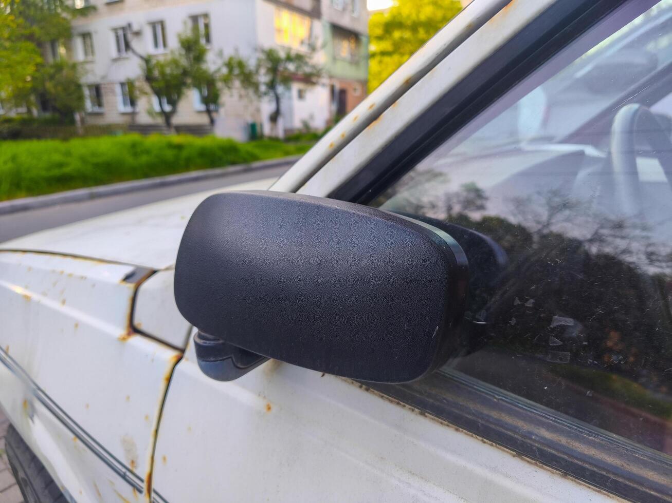 A car's side mirror is covered in black frost. The car is parked on a street with a building in the background photo