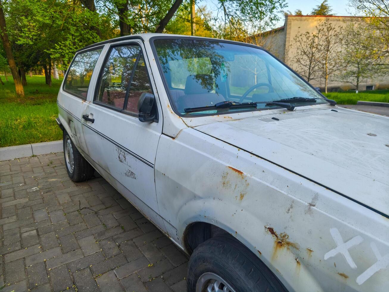 A white car with a black stripe on the side is parked on a brick road. The car is old and has a rustic appearance photo