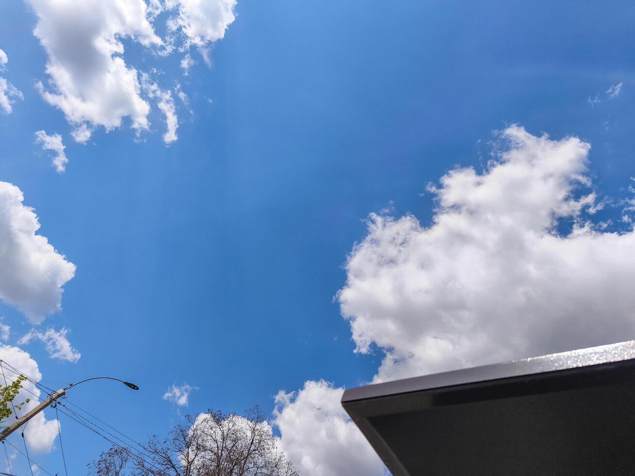 A blue sky with a few clouds and a house in the background. The sky is clear and bright, and the clouds are scattered throughout the sky. The house is located in the background, and it is a small photo