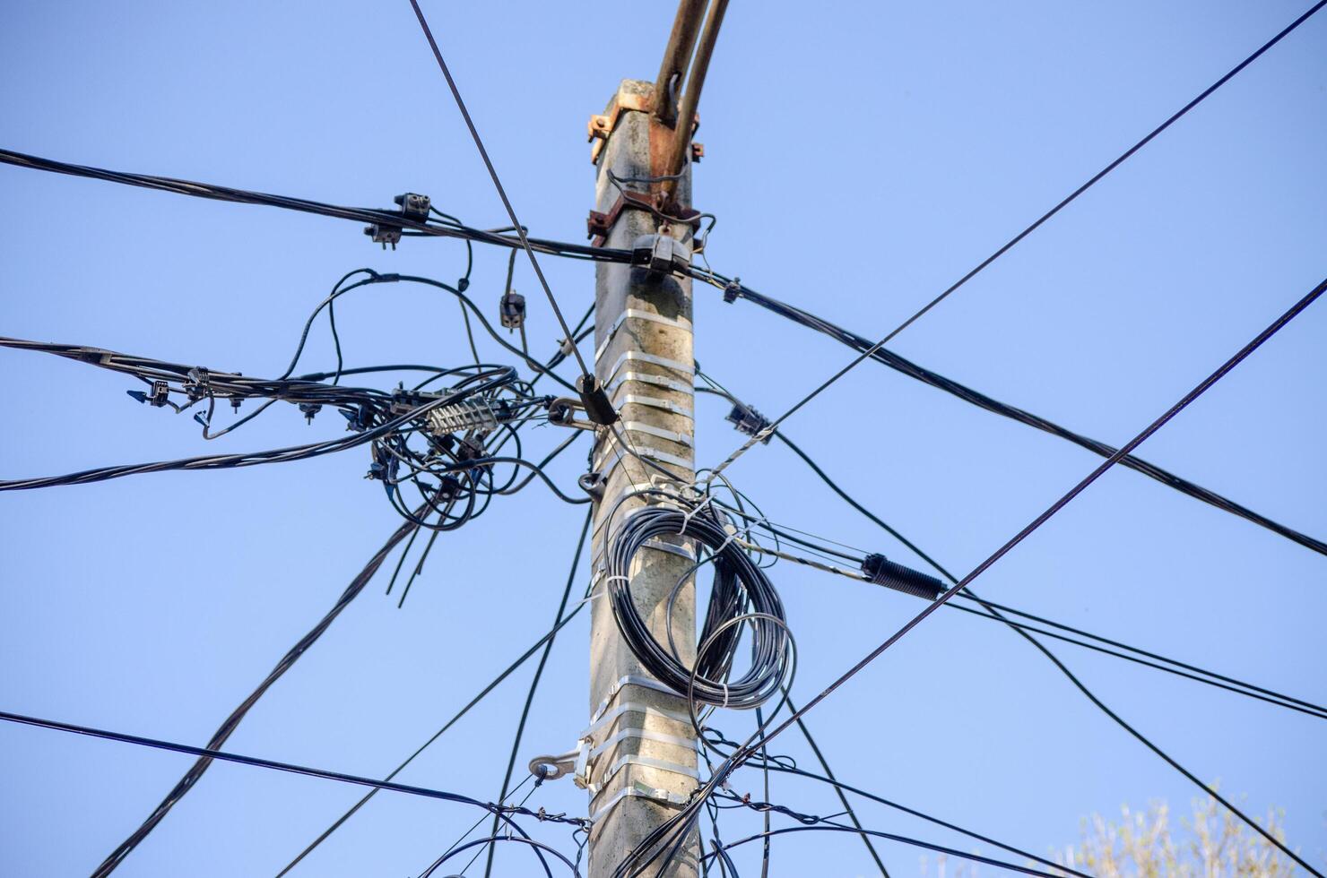 A power line pole with wires hanging from it. The wires are tangled and twisted. The sky is clear and blue photo