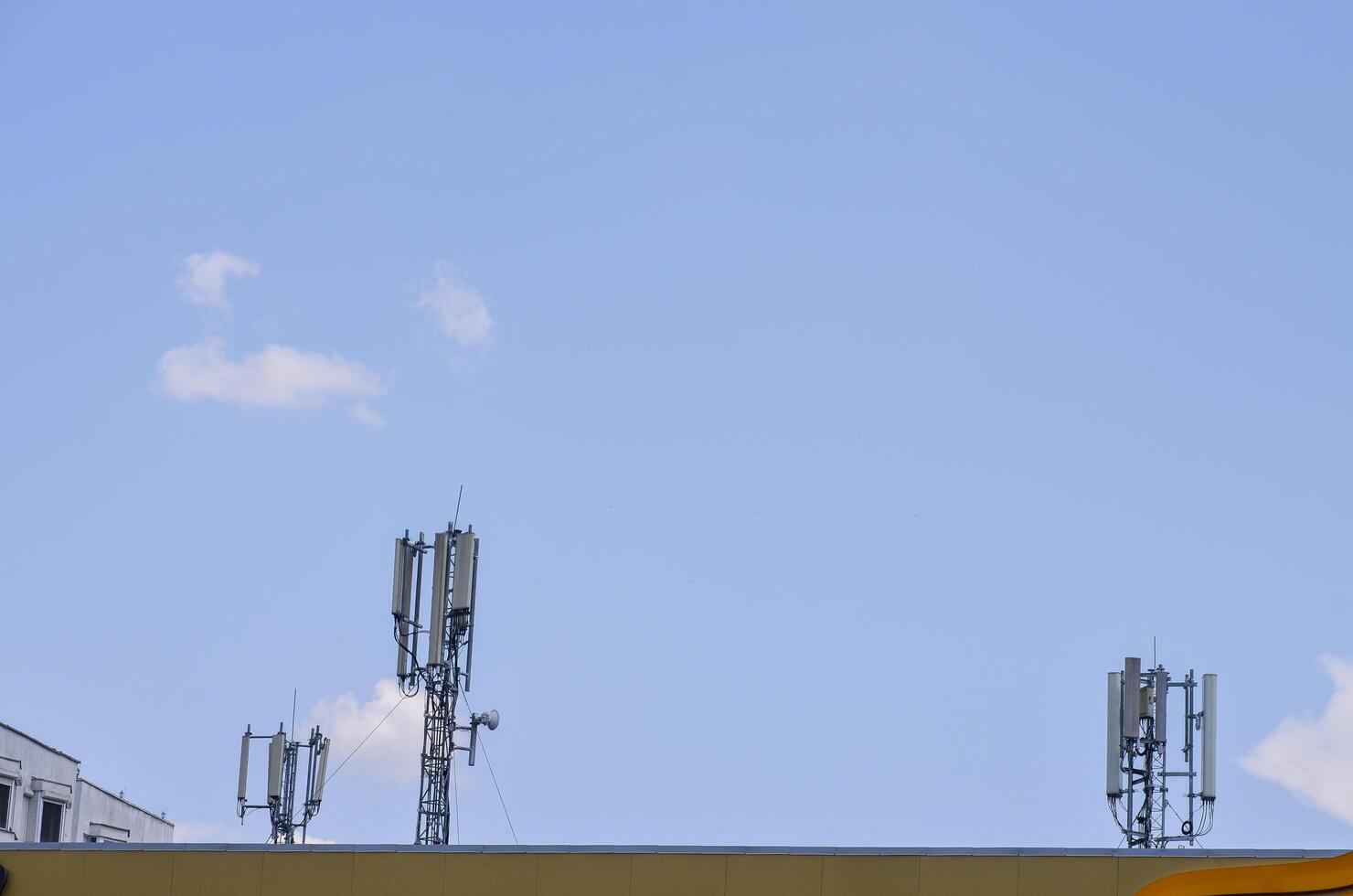 A row of cell phone towers are on top of a building. The sky is clear and blue photo
