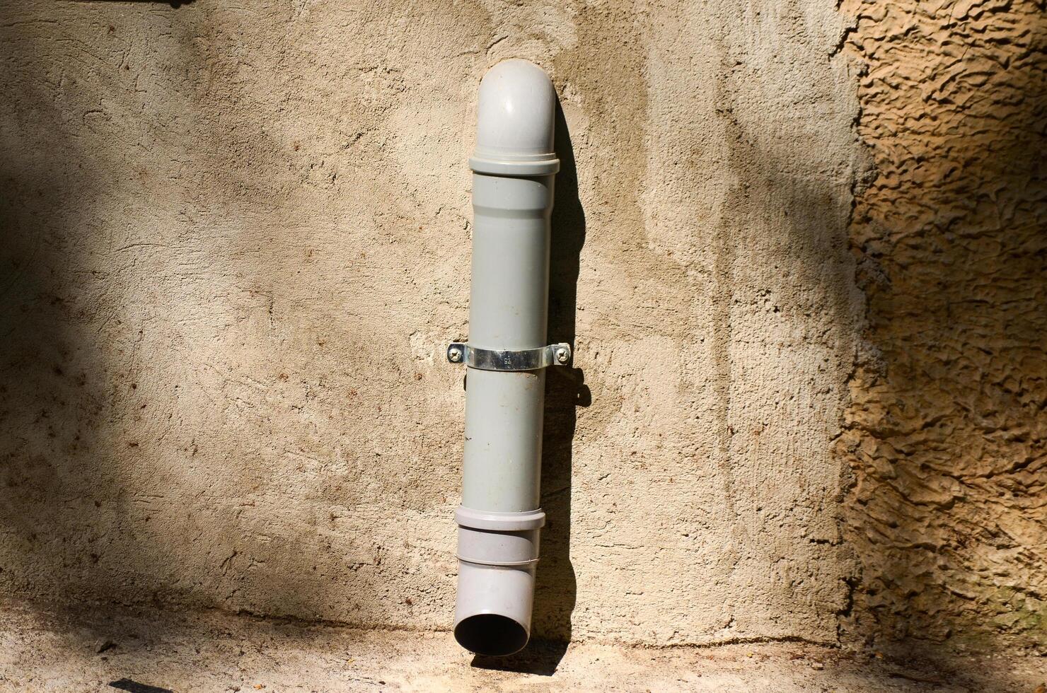 A pipe is leaning against a wall. The pipe is white and has a silver cap. The wall is made of concrete photo