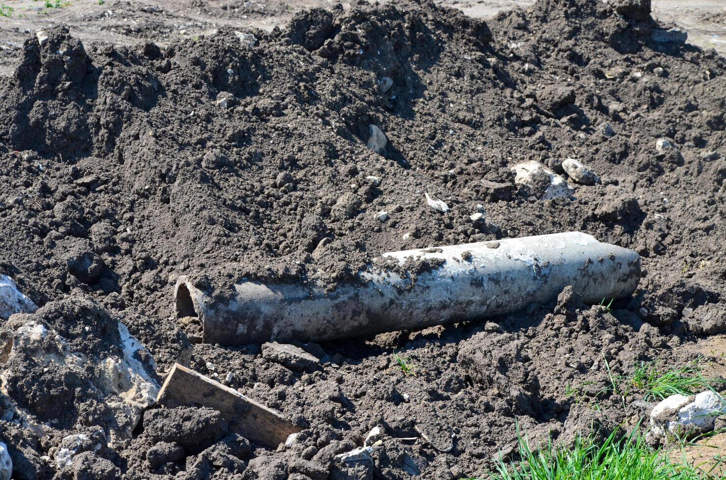 A pipe is laying on the ground in a muddy field. The pipe is covered in dirt and debris, and it is old and rusted. Scene is one of neglect and decay photo