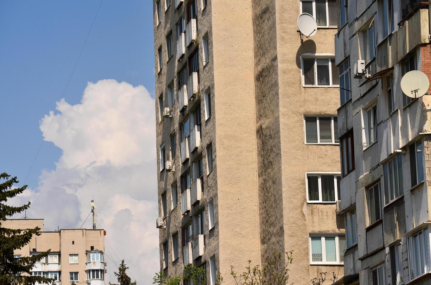 A large building with a lot of windows and a satellite dish on the roof. The sky is cloudy and the sun is shining photo