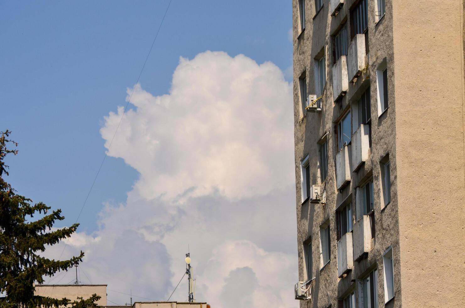 A building with a large cloud in the sky. The cloud is white and fluffy. The building is tall and has many windows photo